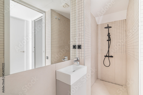 Interior of modern bathroom with beige tiles  shower and small sink