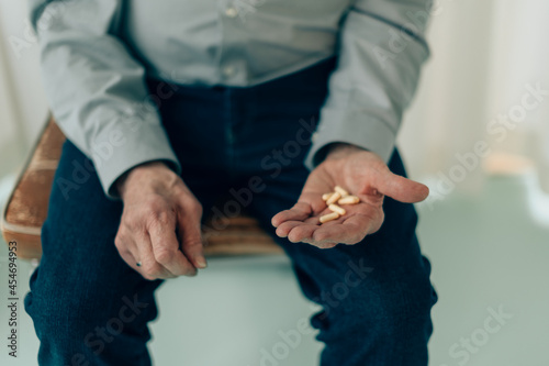 midsection of senior man sitting on chair holding medicine pills in palm - fucus on fingers