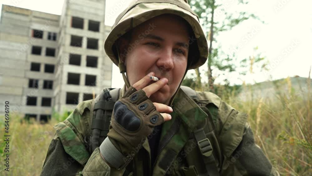 man in uniform smokes a cigarette while sitting on the ground man in uniform smokes a cigarette while sitting on the ground