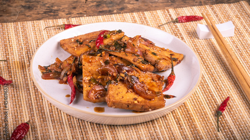 Spicy fried tofu with onions in a plate with chopsticks, close-up