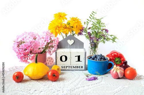 Calendar for September 1 : the name of the month in English, cubes with the numbers 0 and 1, ripe vegetables, bouquets of various flowers, blueberries in a blue cup on a gray napkin, white background photo