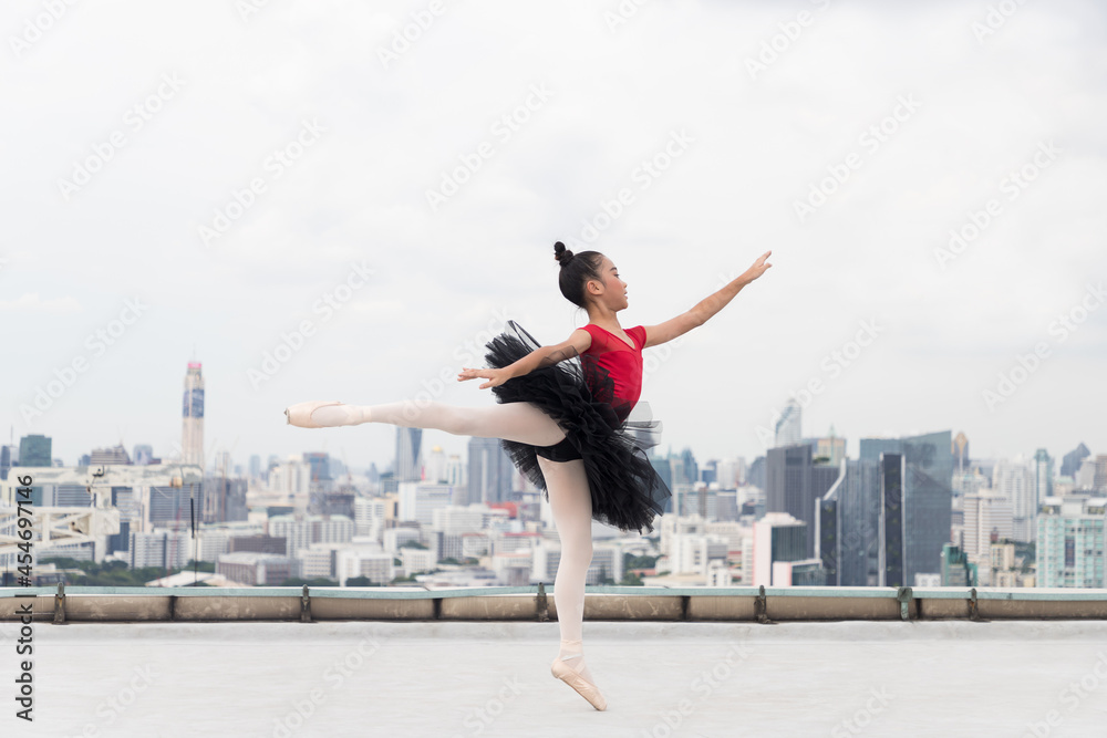 Asian ballerina ballet girl in red, black dress dancing on rooftop with cityscape view background. Young ballerina ballet girl dancing by stretching arms and leg on rooftop Asian ballerina ballet girl in red, black dress dancing on rooftop with cityscape view background. Young ballerina ballet girl dancing by stretching arms and leg on rooftop