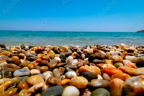 Selective focus of pebbles on the seashore and wavy sea on the background. Pebble sea shore. Vacation, holiday, tourism background.