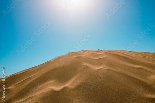 Fototapeta Naklejka Na Ścianę i Meble -  Sand dunes and clear blue sky on the background with sun. Desert, beach, summer and hot weather theme. Sand dunes background. Desert background.