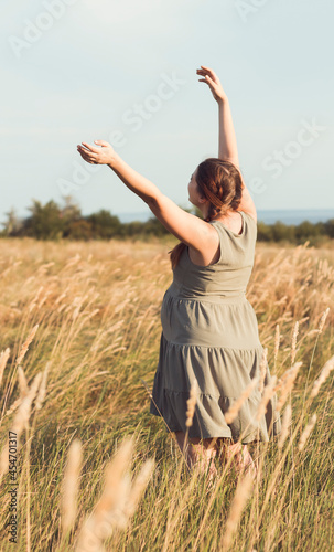 young beautiful pregnant woman walks in field among dry fluffy grass at sunset, relaxation on summer nature, preparation for childbirth and happy, healthy motherhood