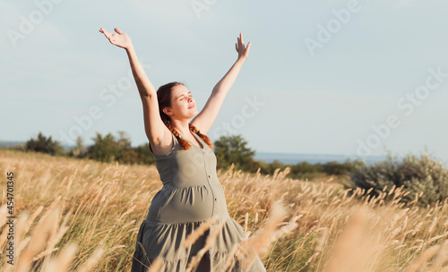 beautiful pregnant woman walks in field among dry fluffy grass enjoying sunset, relaxation on summer nature, preparation for childbirth and happy, healthy motherhood