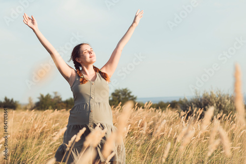 beautiful pregnant woman walks in field among dry fluffy grass enjoying sunset, relaxation on summer nature, preparation for childbirth and happy, healthy motherhood