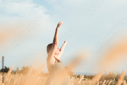 young beautiful pregnant woman walks in field among dry fluffy grass at sunset, relaxation on summer nature, preparation for childbirth and happy, healthy motherhood