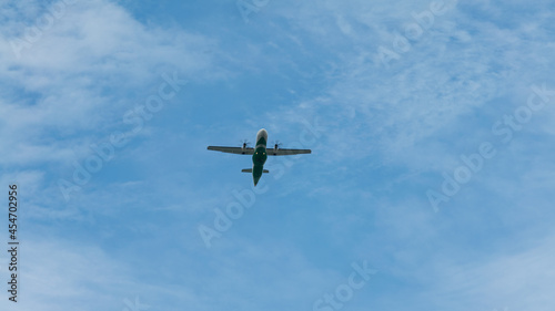 View of propeller plane flying low with blue sky and clouds at background.