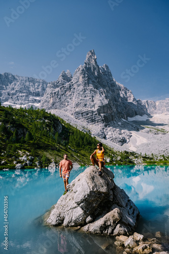 Morning with clear sky on Lago di Sorapis in the Italian Dolomites, milky blue lake Lago di Sorapis, Lake Sorapis, Dolomites, Italy. Couple man and woman mid age walking by the lake in the mountains  photo