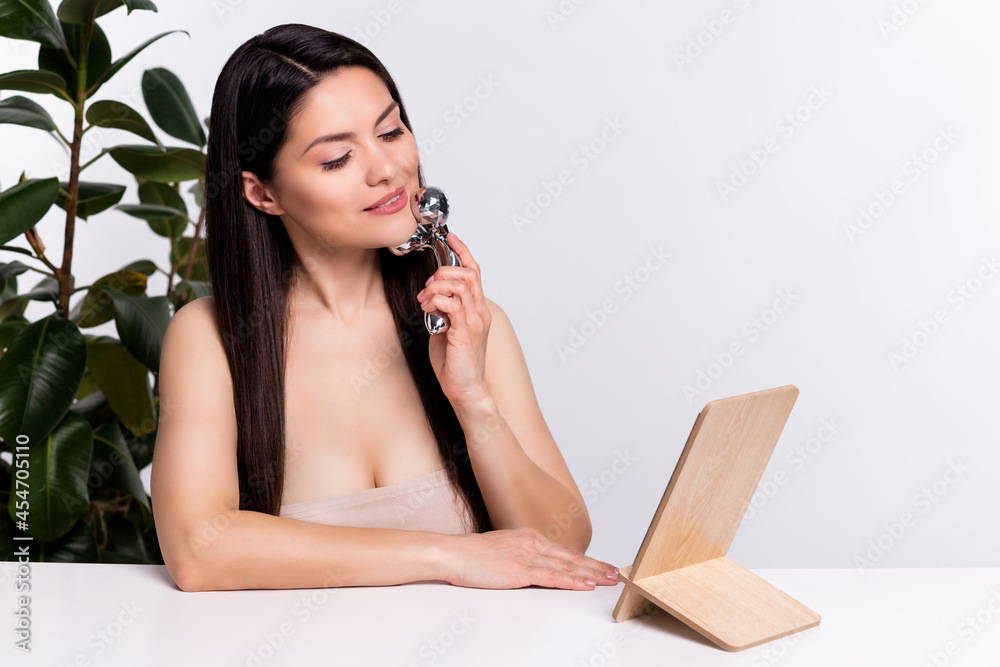 Photo portrait woman long brunette hair smiling looking at mirror doing face massage isolated white color background Photo portrait woman long brunette hair smiling looking at mirror doing face massage isolated white color background