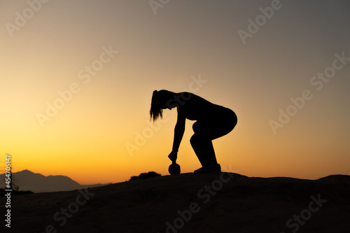 Silueta de deportista entrenando con un kettlebell en la montaña, con el atardecer y espacio para texto.  © Ezequiel Martínez