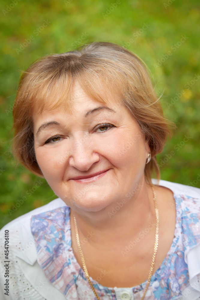 Portrait of an elderly or middle-aged woman with a green background in a park or forest in nature Portrait of an elderly or middle-aged woman with a green background in a park or forest in nature