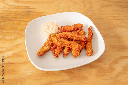 serving of chicken fingers battered with flour, egg and breadcrumbs with mayonnaise sauce on a white plate
