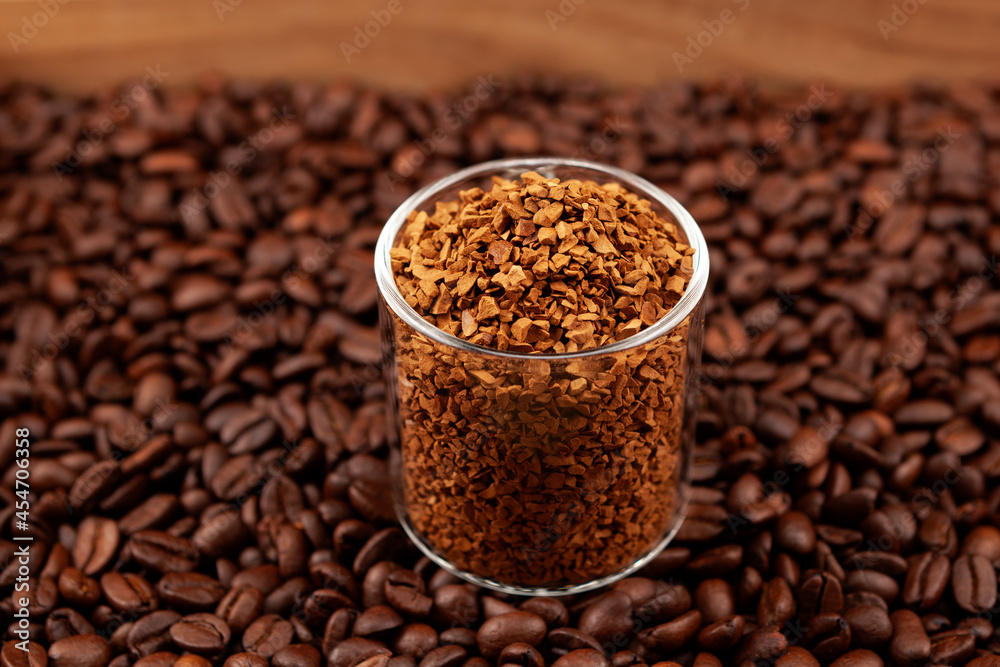 Instant, freeze-dried or granulated coffee in glass on background of roasted coffee beans. Used to make a cold Dalgon coffee drink. Side view, closeup, selective focus Instant, freeze-dried or granulated coffee in glass on background of roasted coffee beans. Used to make a cold Dalgon coffee drink. Side view, closeup, selective focus