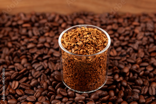 Instant, freeze-dried or granulated coffee in glass on background of roasted coffee beans. Used to make a cold Dalgon coffee drink. Side view, closeup, selective focus