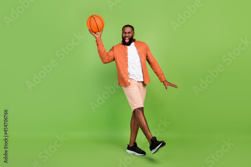 Full body photo of impressed millennial brunet guy play wear shirt shorts shoes isolated on green background