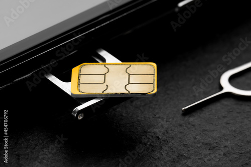 Photography SIM card, mobile phone and ejector on black table, closeup