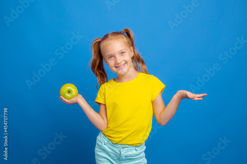 a little girl holds an apple on a blue background