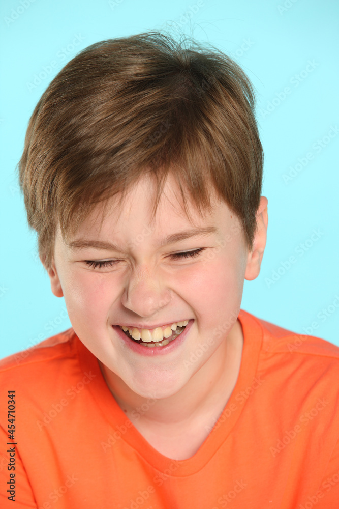 Close-up portrait: a handsome developed cheerful teenage boy in an orange T-shirt laughs to tears, closing his eyes. Close-up portrait: a handsome developed cheerful teenage boy in an orange T-shirt laughs to tears, closing his eyes.