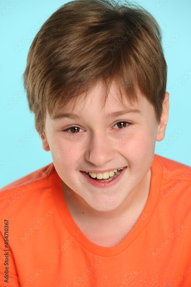 Close-up portrait: a handsome developed cheerful teenage boy in an orange T-shirt laughs to tears and looks eye to eye. Close-up portrait: a handsome developed cheerful teenage boy in an orange T-shirt laughs to tears and looks eye to eye.