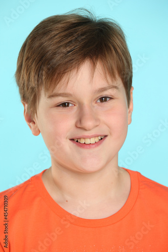 Close-up portrait: a handsome developed cheerful teenage boy in an orange T-shirt smiles and looks eye to eye.