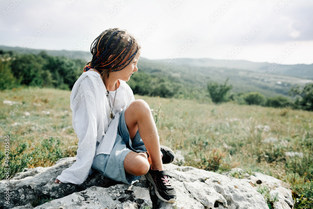 A child walks in the mountains, sitting on a stone and looking into the distance