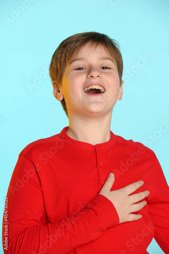 In the portrait, a fashionable, cheerful teenage boy in a red sweater smiles broadly and theatrically thanks. photo