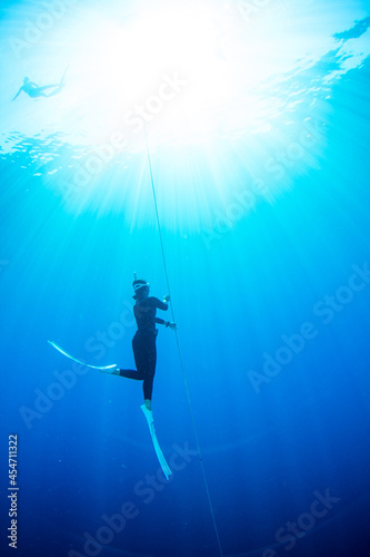 Young freediver asian woman with fins glides and amazing sun rays. Freediving underwater in Amed, Bali Indonesia.
