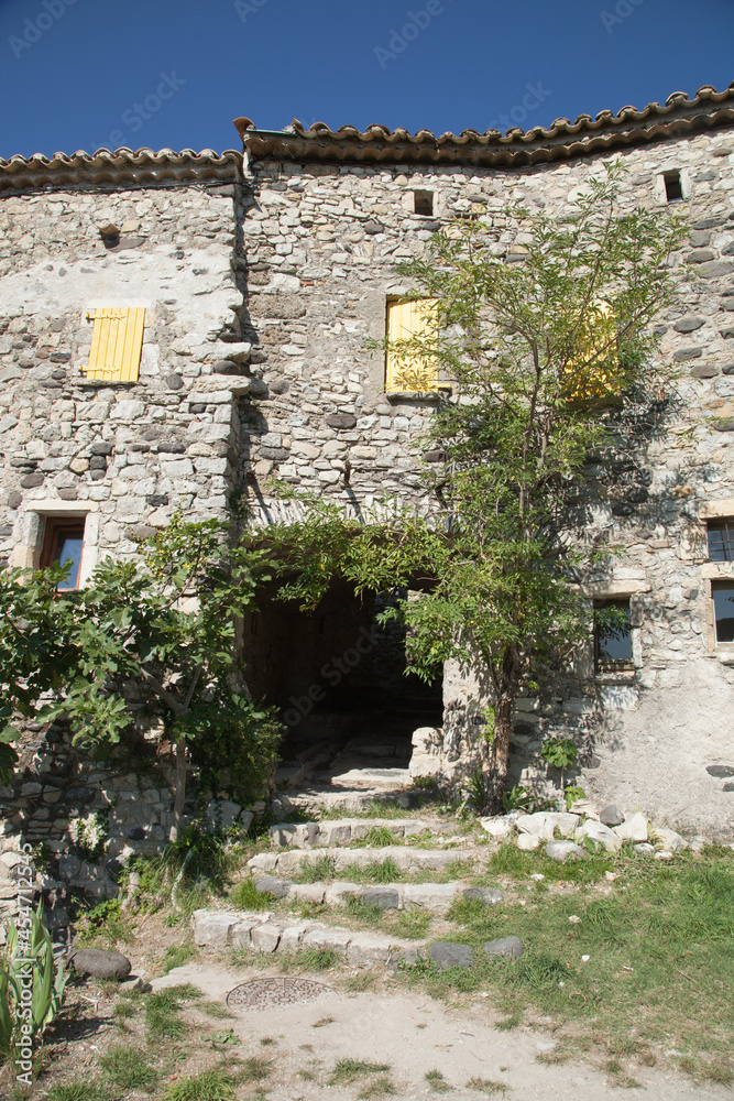 Vieille maison aux volets jaunes fermés avec une arcade couverte dans le village de Saint-Thomé en Ardèche