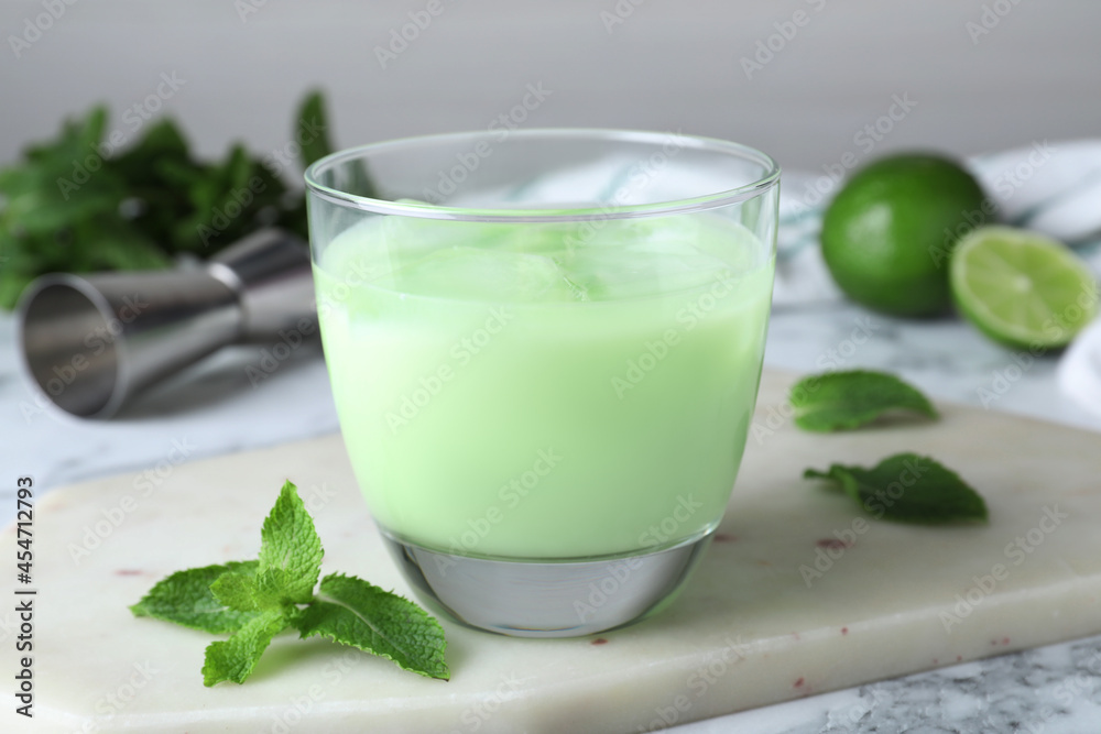 Delicious mint liqueur with ice cubes and green leaves on white marble table, closeup Delicious mint liqueur with ice cubes and green leaves on white marble table, closeup