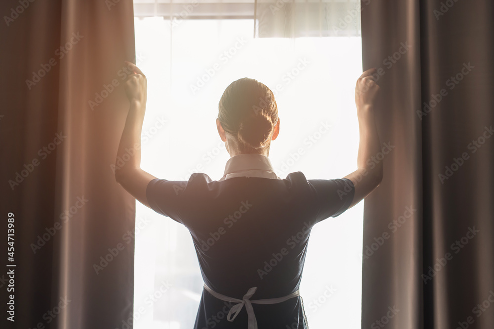 back view of maid adjusting curtains in hotel room - obrazy, fototapety, plakaty 