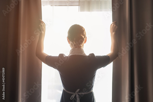 back view of maid adjusting curtains in hotel room photo