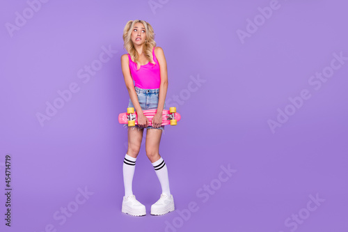 Full length body size view of lovely worried girl holding skate biting lip copy space isolated over bright purple violet color background
