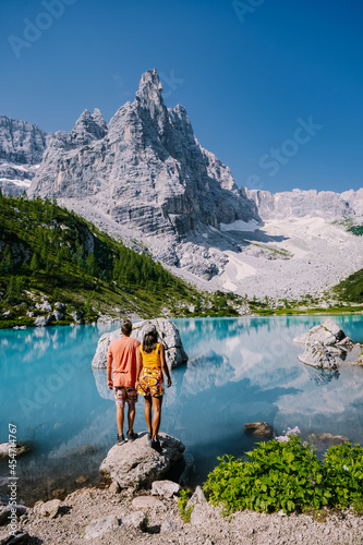 Morning with clear sky on Lago di Sorapis in the Italian Dolomites, milky blue lake Lago di Sorapis, Lake Sorapis, Dolomites, Italy. Couple man and woman mid age walking by the lake in the mountains  photo