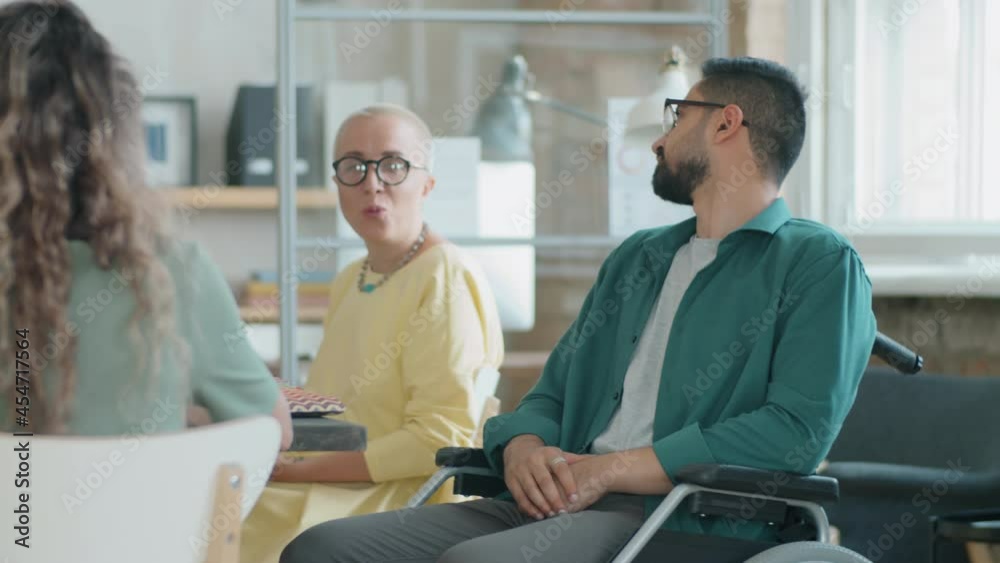 Young middle eastern businessman with disability sitting in wheelchair and speaking with multiethnic colleagues during office meeting Young middle eastern businessman with disability sitting in wheelchair and speaking with multiethnic colleagues during office meeting