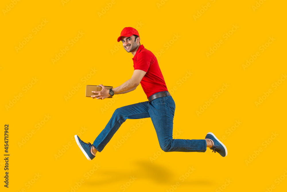 Portrait of a young delivery boy running carrying a box on plain backdrop.