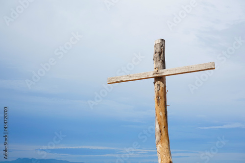 A cross sign made by old wood is at the right side of photo. White and blue sky in the background.  A religious symbol, crucifix, death and spiritual themes.