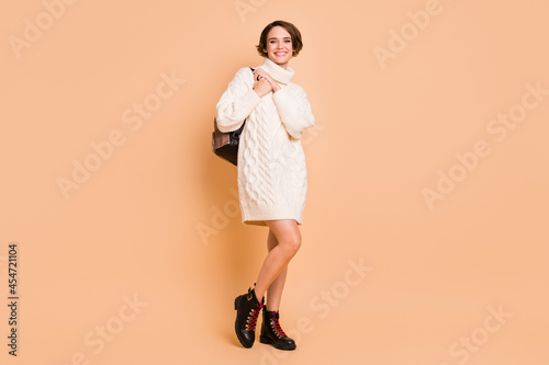 Full length body size photo of female student in white sweater having rucksack smiling isolated on pastel beige color background photo