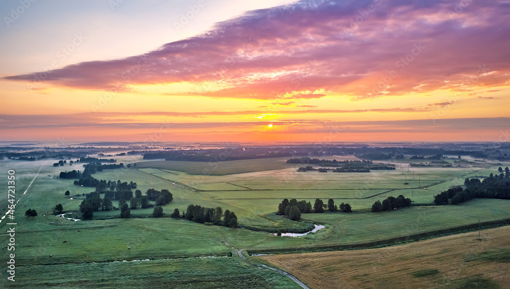 Dramatic summer sunrise. Panorama misty landscape. Foggy Morning on river aerial view. Green fields and meadows