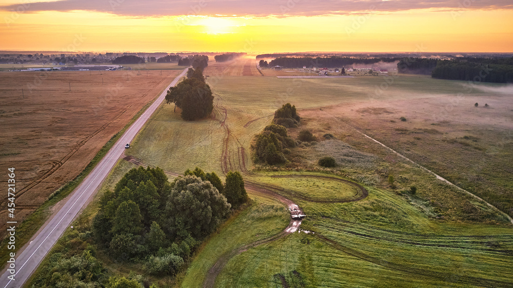 Dramatic summer sunrise. Panorama misty landscape. Foggy Morning over Green fields and meadows aerial view. Asphalt rural empty road