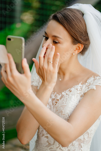 bride wipes face with matting cloth and uses phone instead of mirror. 