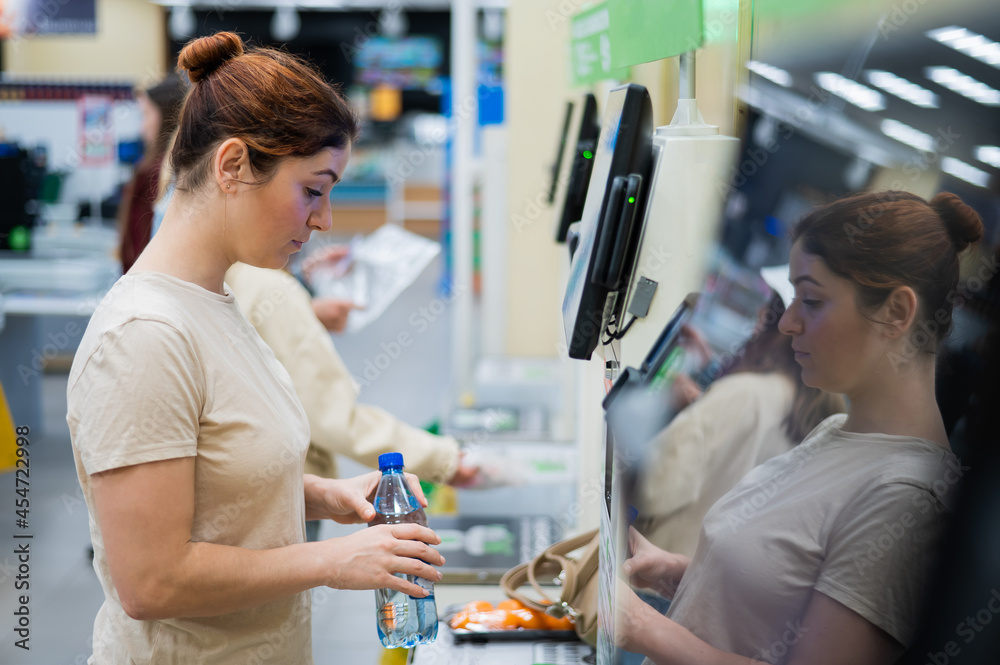 Obraz premium A frustrated woman uses a self-checkout counter. The girl does not understand how to independently buy groceries in the supermarket without a seller