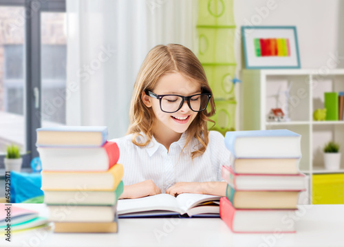 education and school concept - happy smiling student girl in glasses reading book over home background