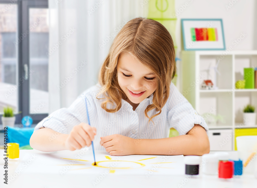 hobby, art and childhood concept - happy smiling girl with brush and colors drawing picture over home room background hobby, art and childhood concept - happy smiling girl with brush and colors drawing picture over home room background