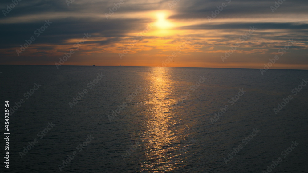 Ocean surface against peaceful cloudy sky with yellow sun. Ocean reflecting sun.