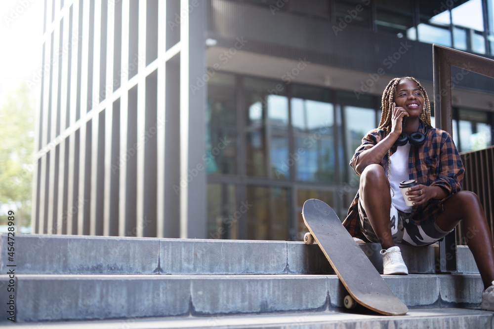 Beautiful african-american woman with skateboard. Young stylish woman with skateboard using the phone outdoors.