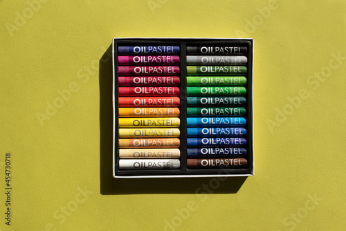 Oil pastels in a box on a green background, top view, drawing materials