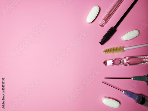 Medical cosmetology. Gloves, syringes, ampoule pills and brushes and eyebrows on a pink background side view