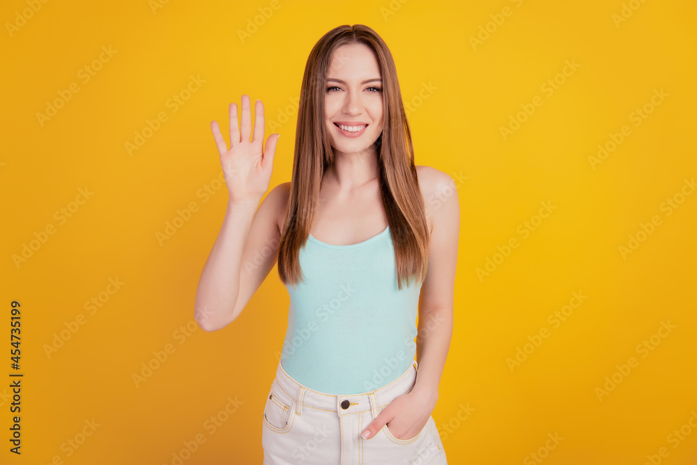 Portrait of friendly cute cheerful lady posing look camera wave hand on yellow background